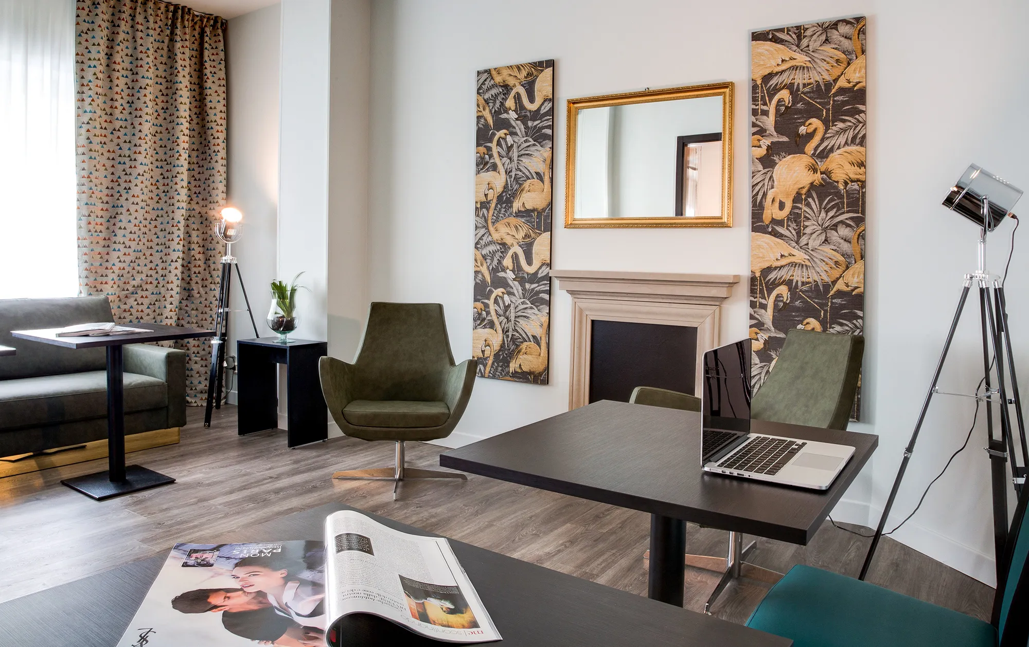 Nell'immagine la sale meeting dell'hotel. Ci sono due tavolini di legno scuro: su quello in primo piano è posata una rivista, su quello dietro c'è un laptop e accanto un faretto. A sinistra si vede un divano con altri tavolini. Accanto al divano c'è un mobiletto con una pianta e un altro faretto. Al centro ci sono due sedie girevoli verdi e sulla parete dietro due quadri verticali, uno specchio e un finto camino.